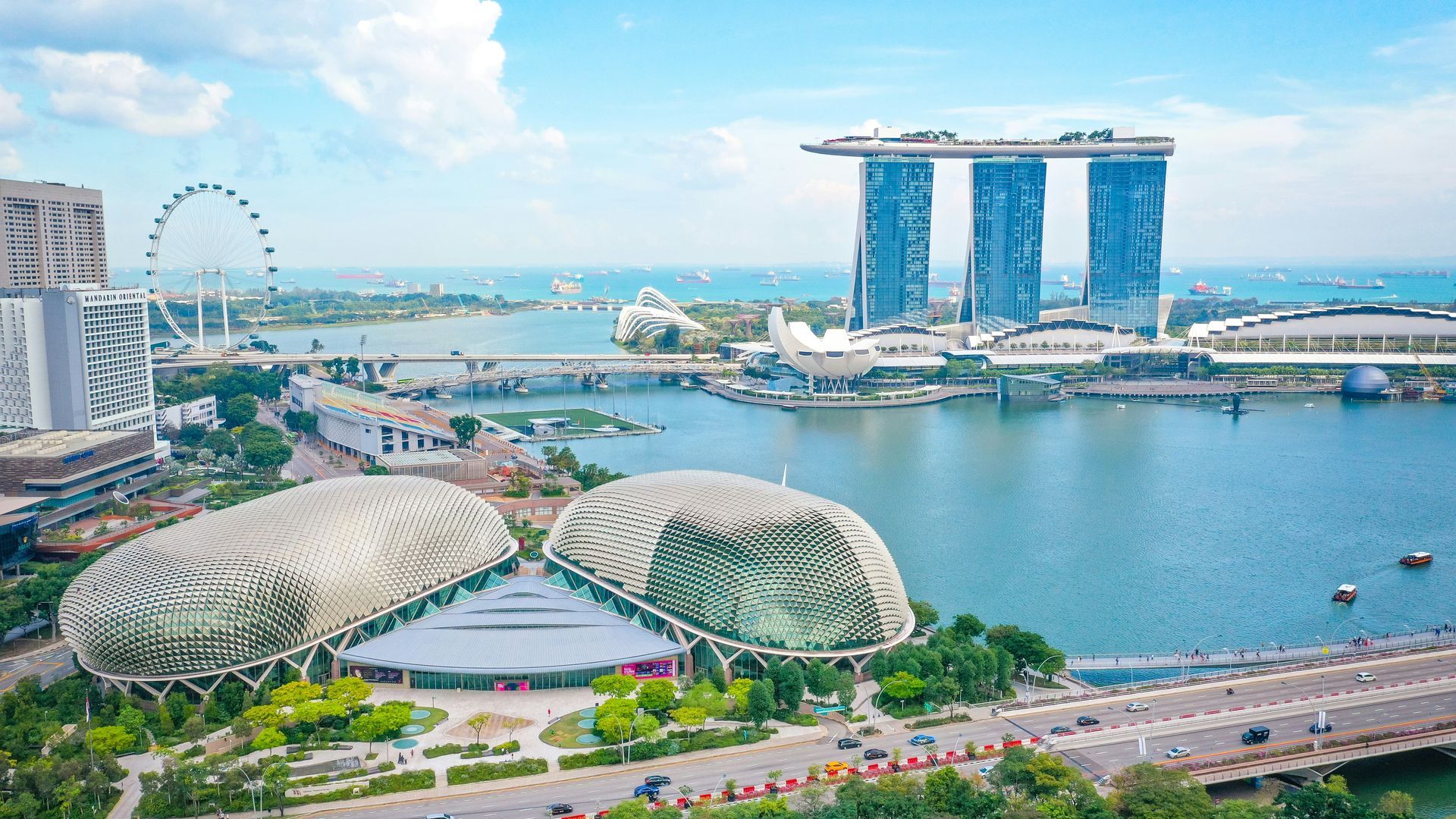 Marina Bay Sands and other buildings line a body of water in Singapore. Bright blue sky.