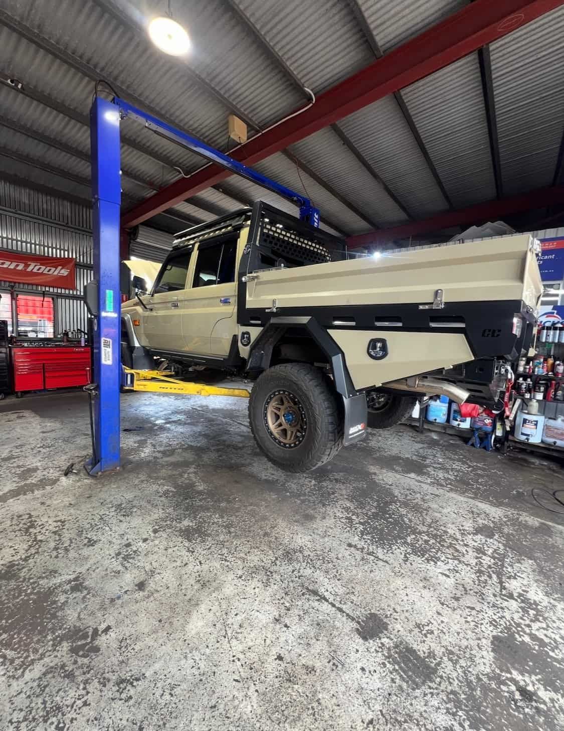 A Brown 4x4 Ute on a lift in a garage — AWS Mechanical in Stuart Park, NT
