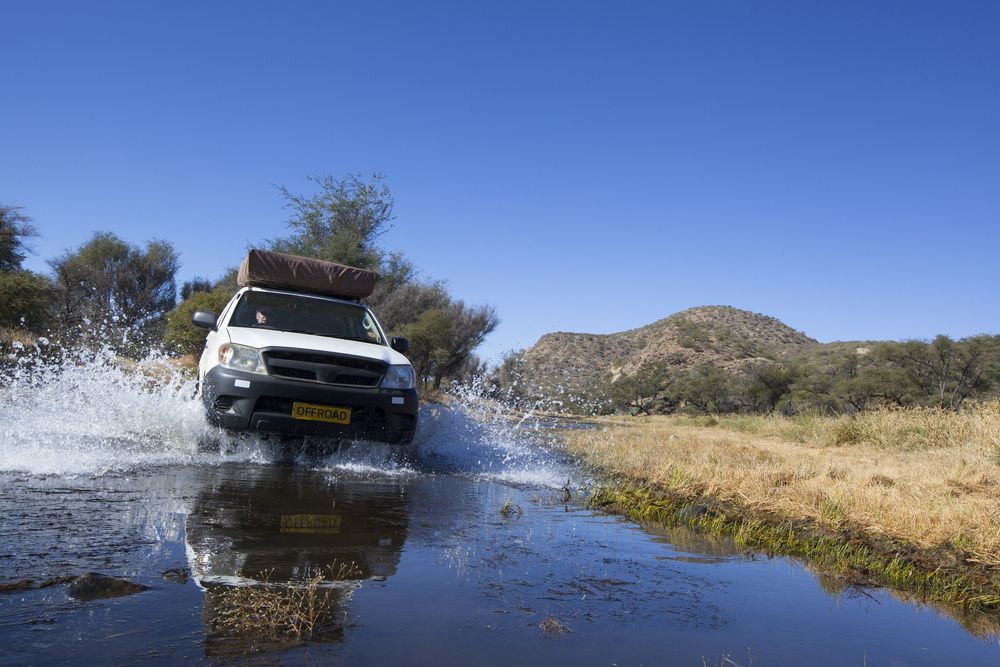 A White SUV With A Roof Tent Driving Through A Shallow Water — AWS Mechanical in Stuart Park, NT