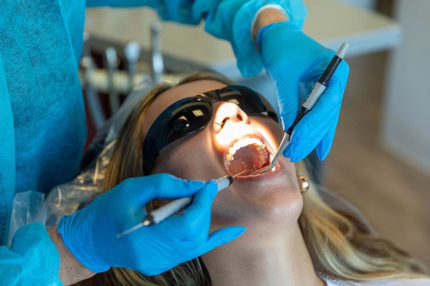 Dentist using blue gloves and tools to examine a patient’s open mouth during a dental procedure