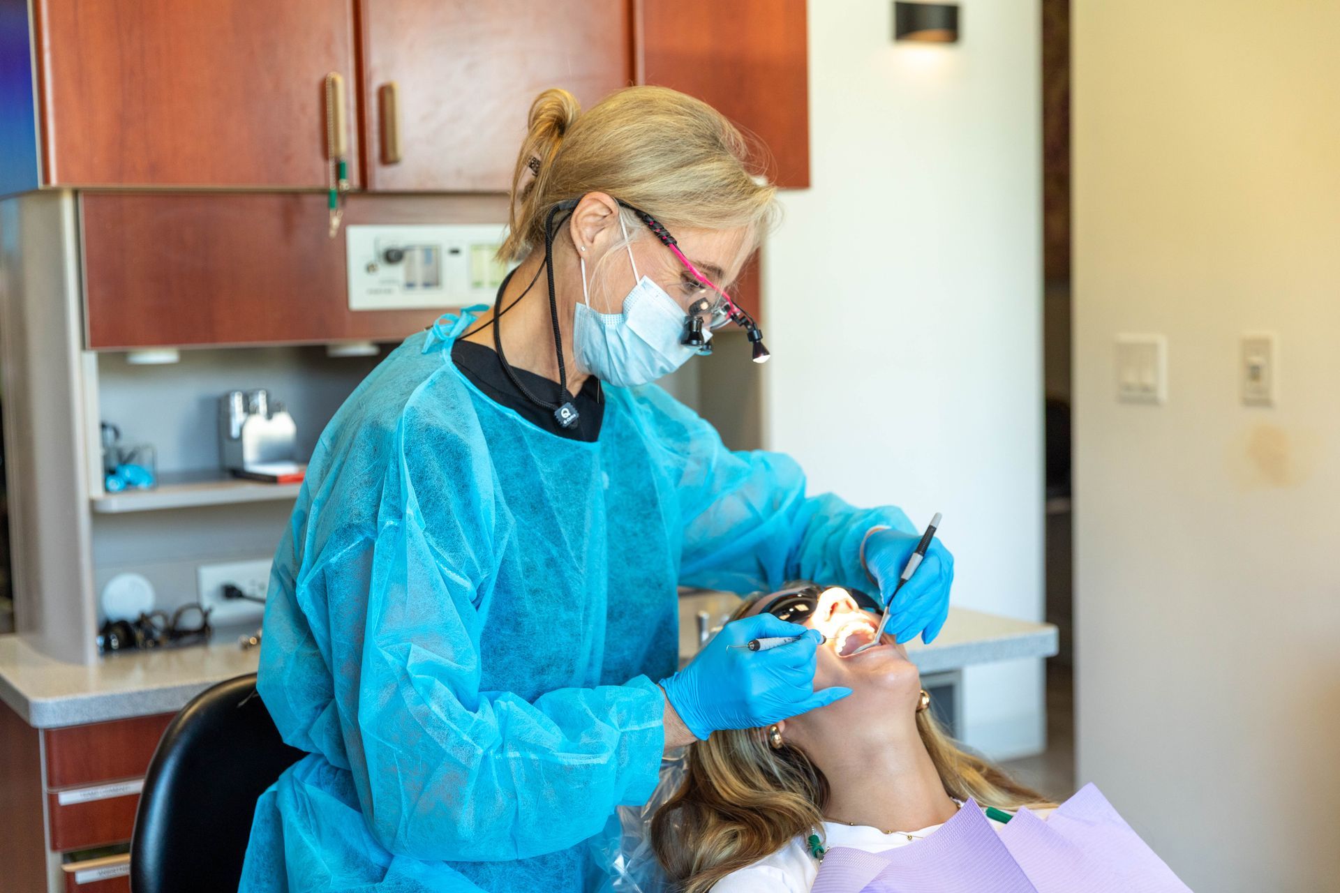 Dentist in blue protective gear examining a patient in a dental office