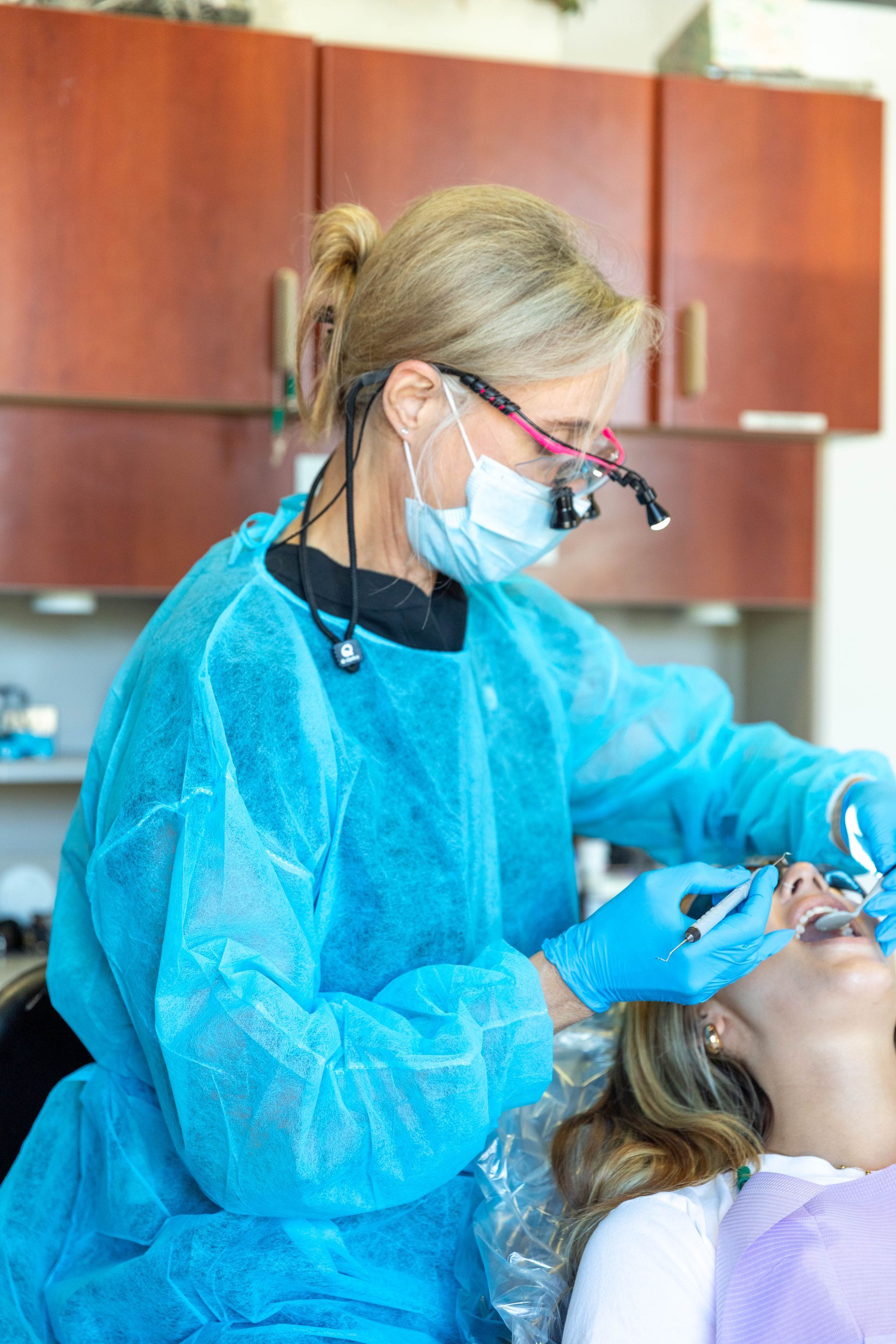 Dentist in blue protective gear examining a patient in a dental chair