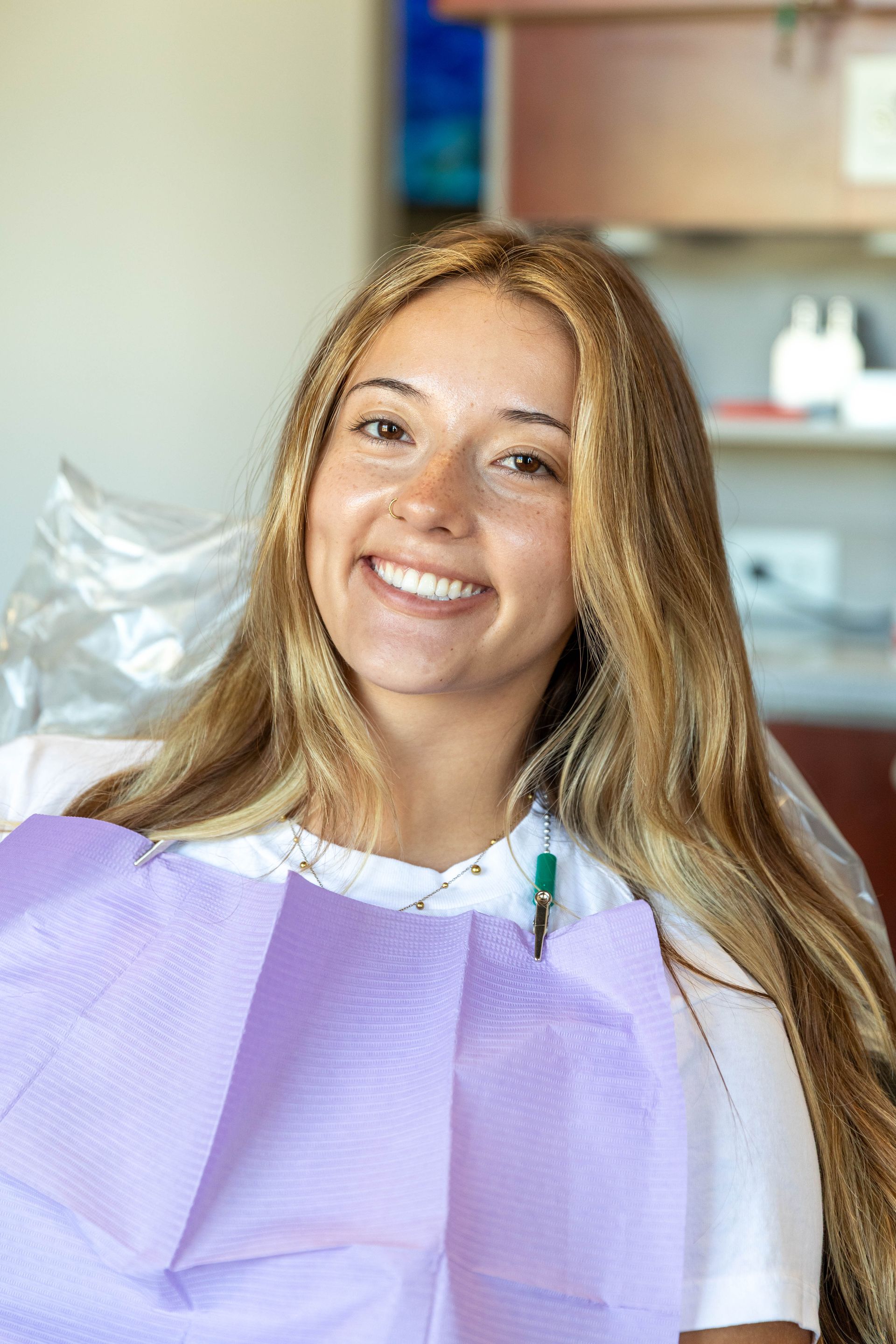 Smiling dental patient in a purple bib seated in a dental chair with clinic equipment behind her