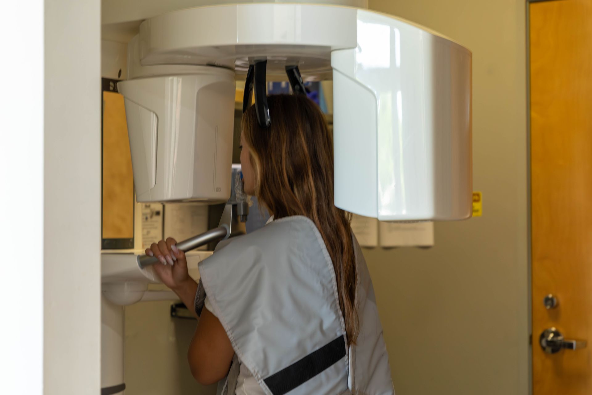 Person standing inside dental X-ray machine, holding a support bar in a clinic.
