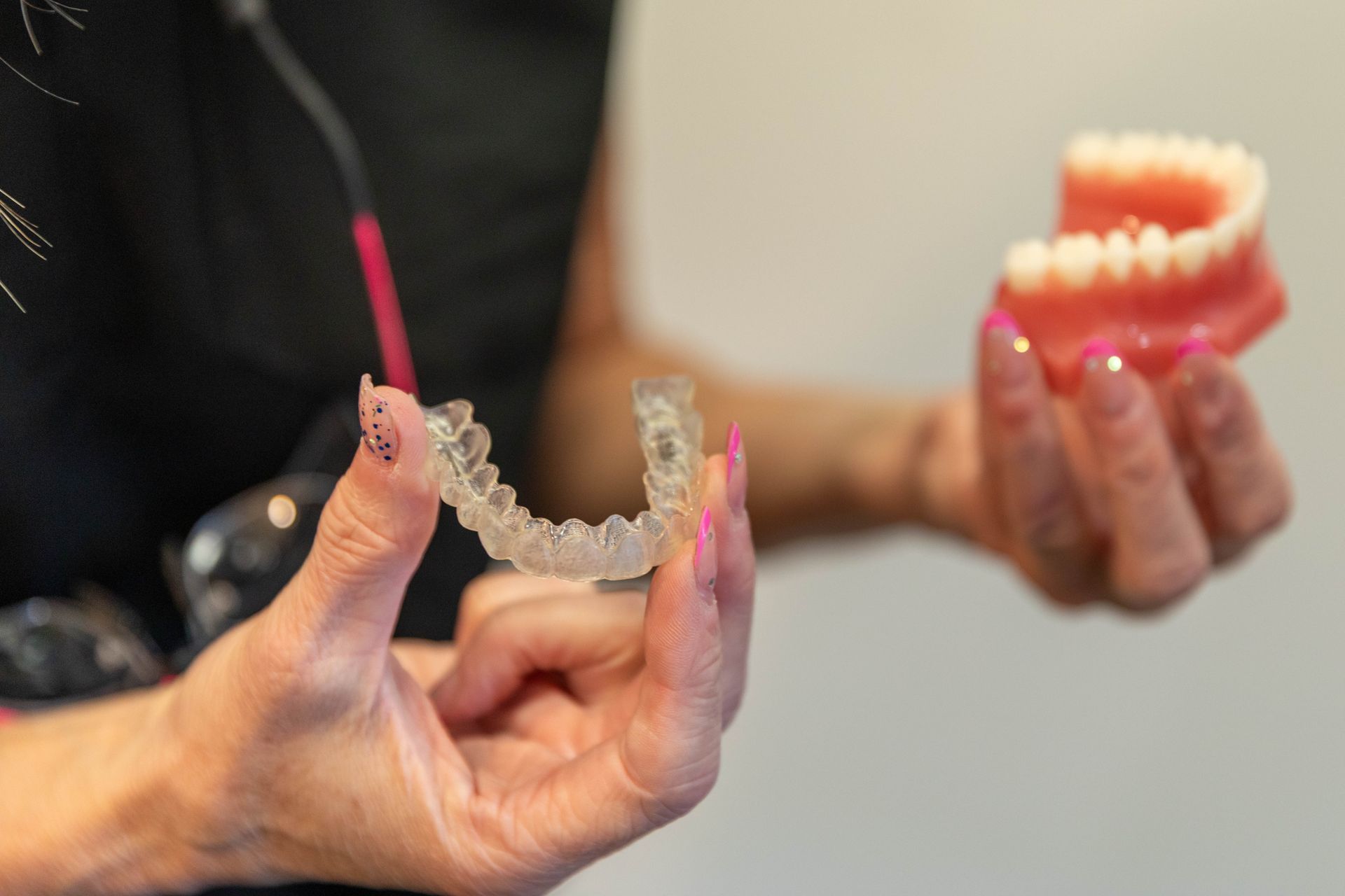 Hands holding clear dental aligners and a pink model jaw during an orthodontic consultation