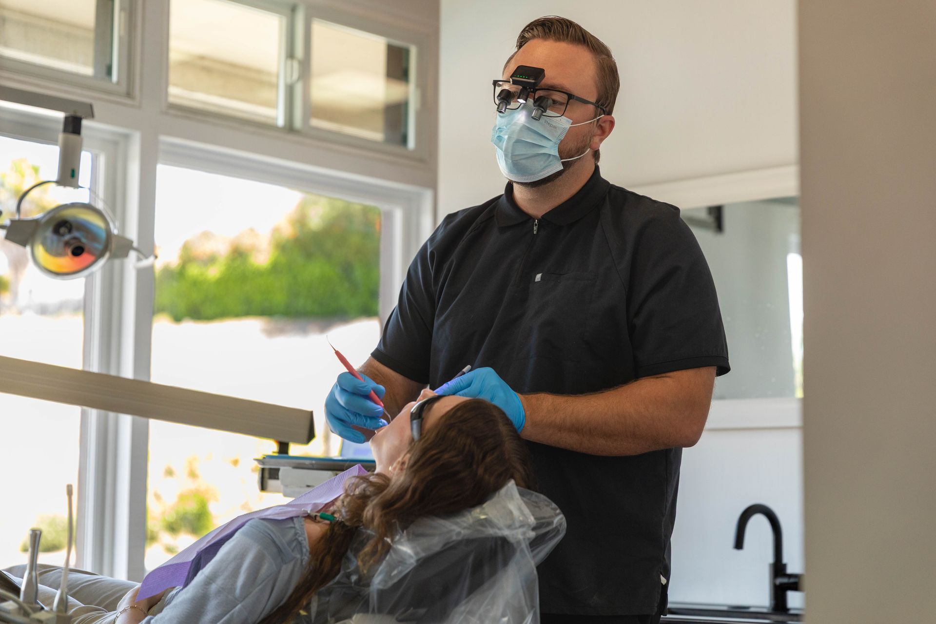 Dentist wearing mask and gloves treating a patient in a bright dental office