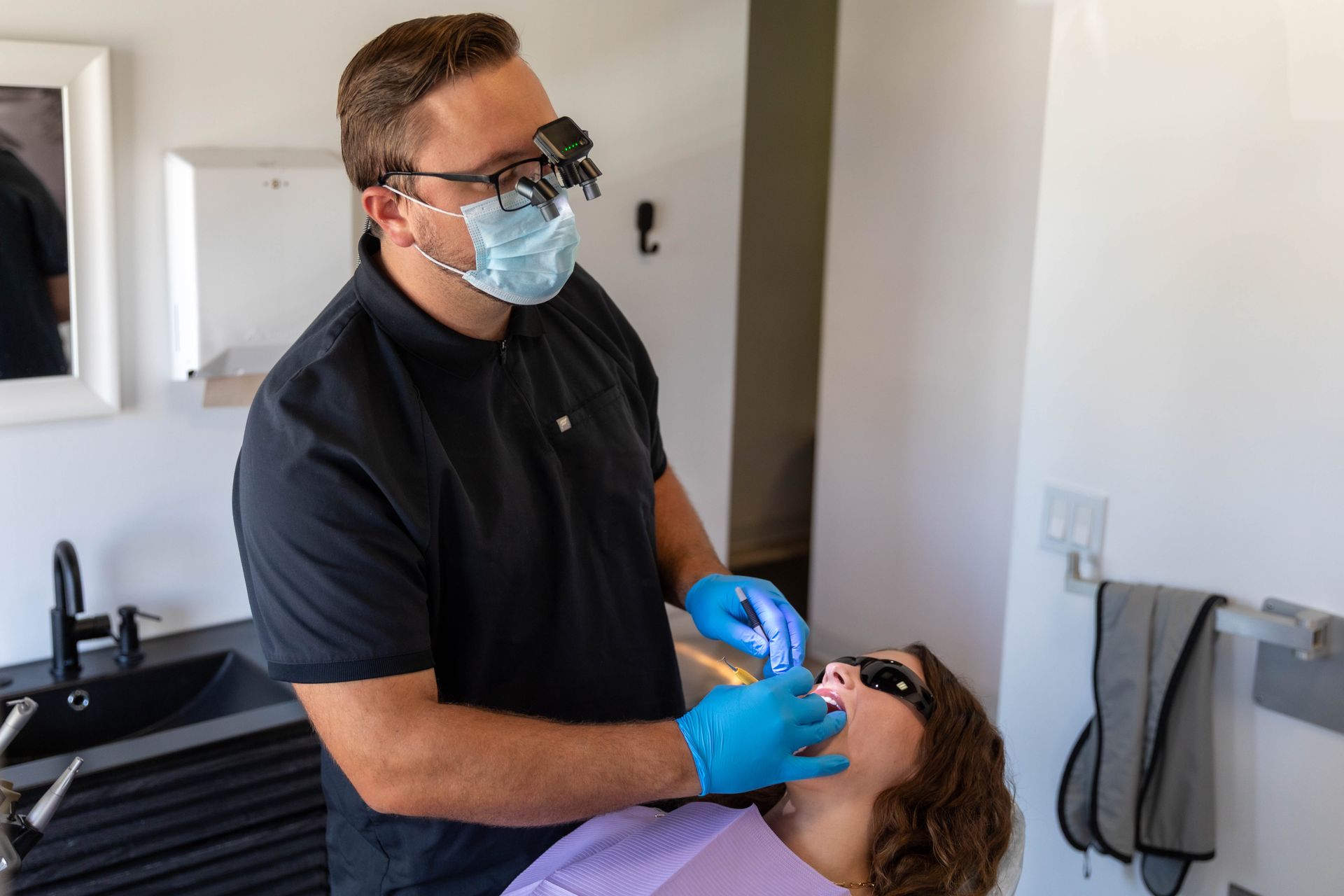 Dentist wearing blue gloves and mask treating a patient in a dental chair