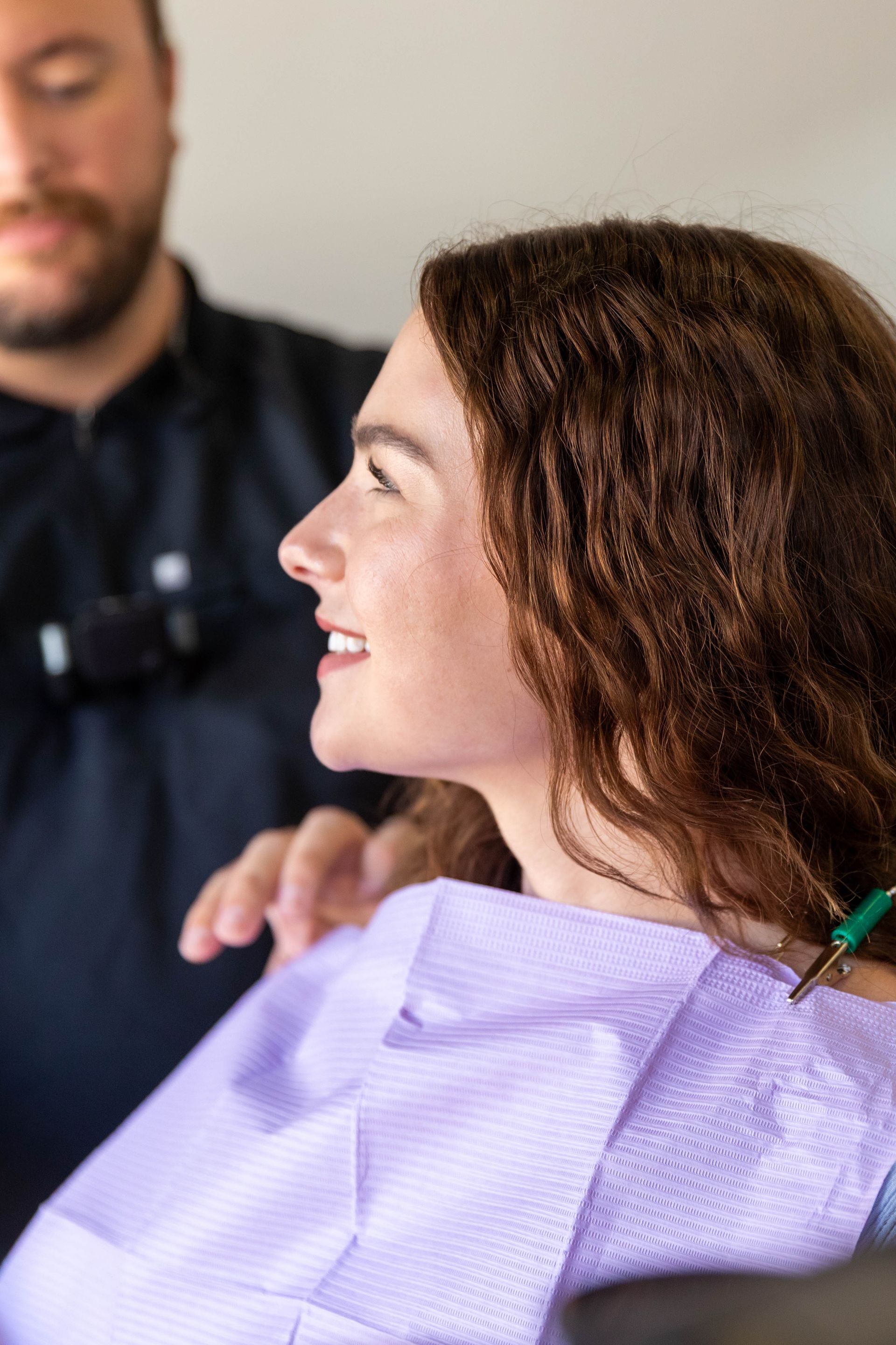 Woman smiling in a salon chair with a purple cape while a stylist stands behind her.