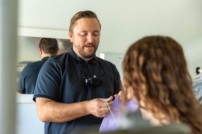 Hair stylist consulting with a client in a salon, holding a comb and wearing a black apron.