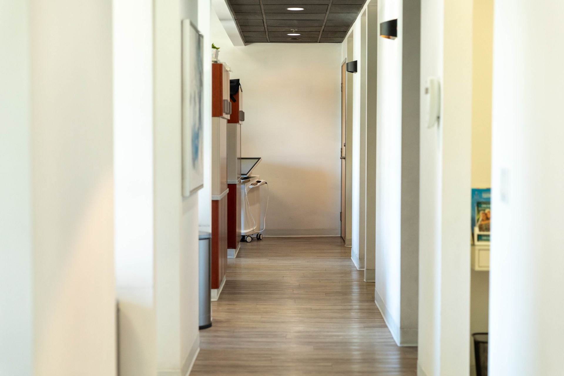 Bright hallway with white walls, wood floor, and a chair at the far end.