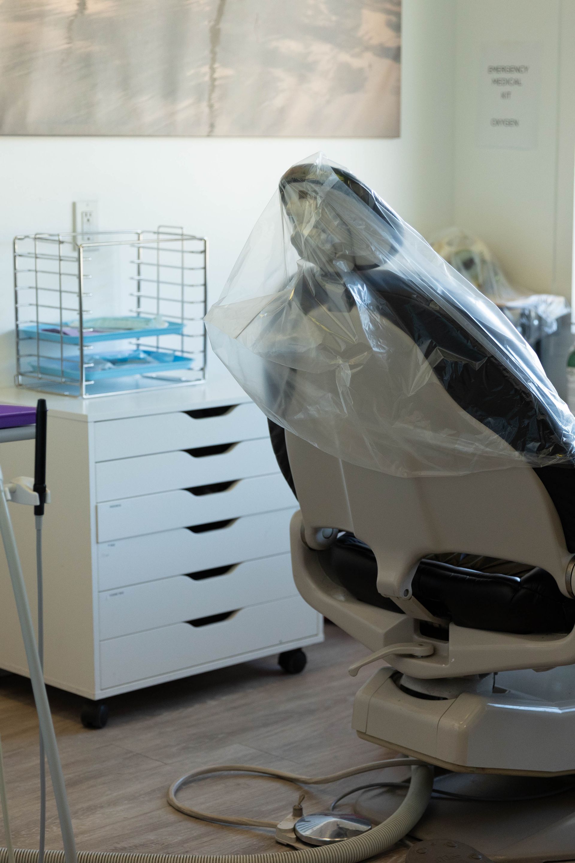 Dental chair wrapped in plastic in a clean clinic room beside a white storage cart