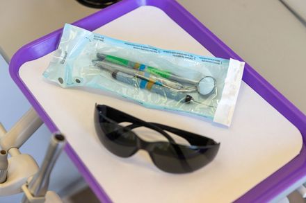 Sunglasses and a sealed dental instrument packet on a small white tray with a purple rim