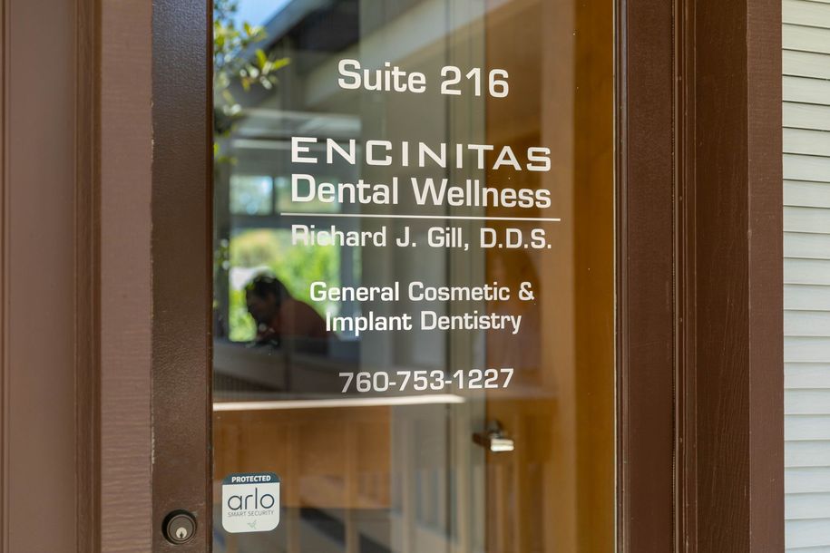 Glass door sign for Encinitas Dental Wellness, Suite 216, with office hours and phone number visible