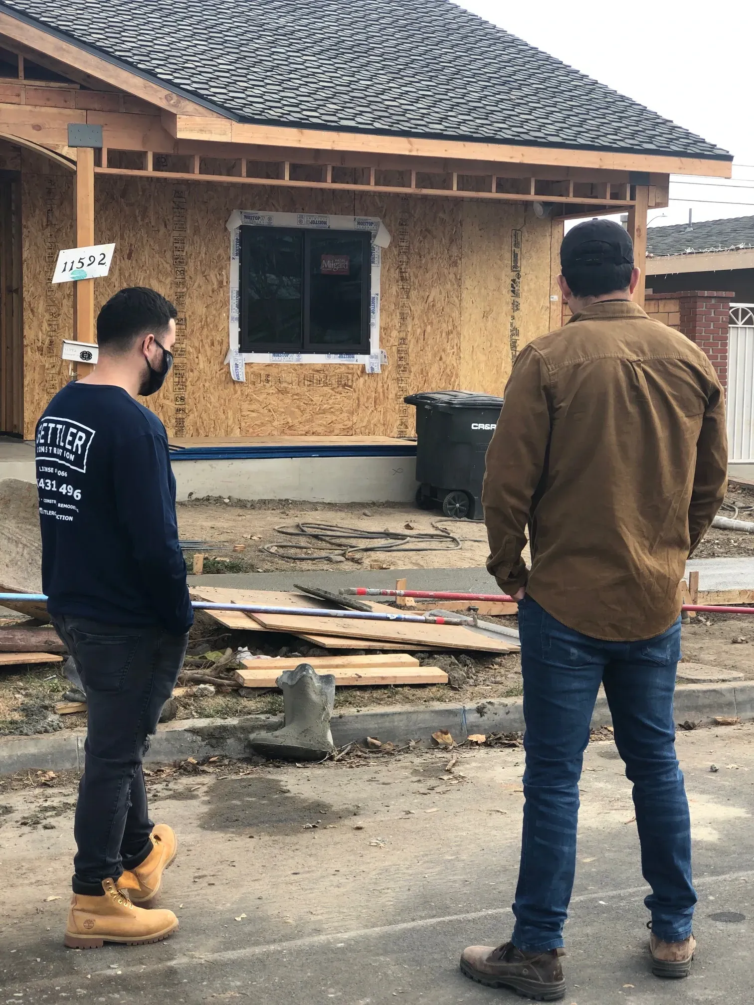 Two men are standing in front of a house under construction.