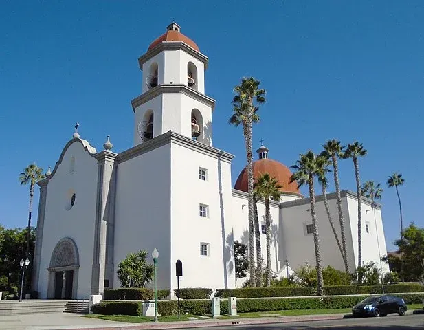 A large white building with a bell tower and palm trees in front of it