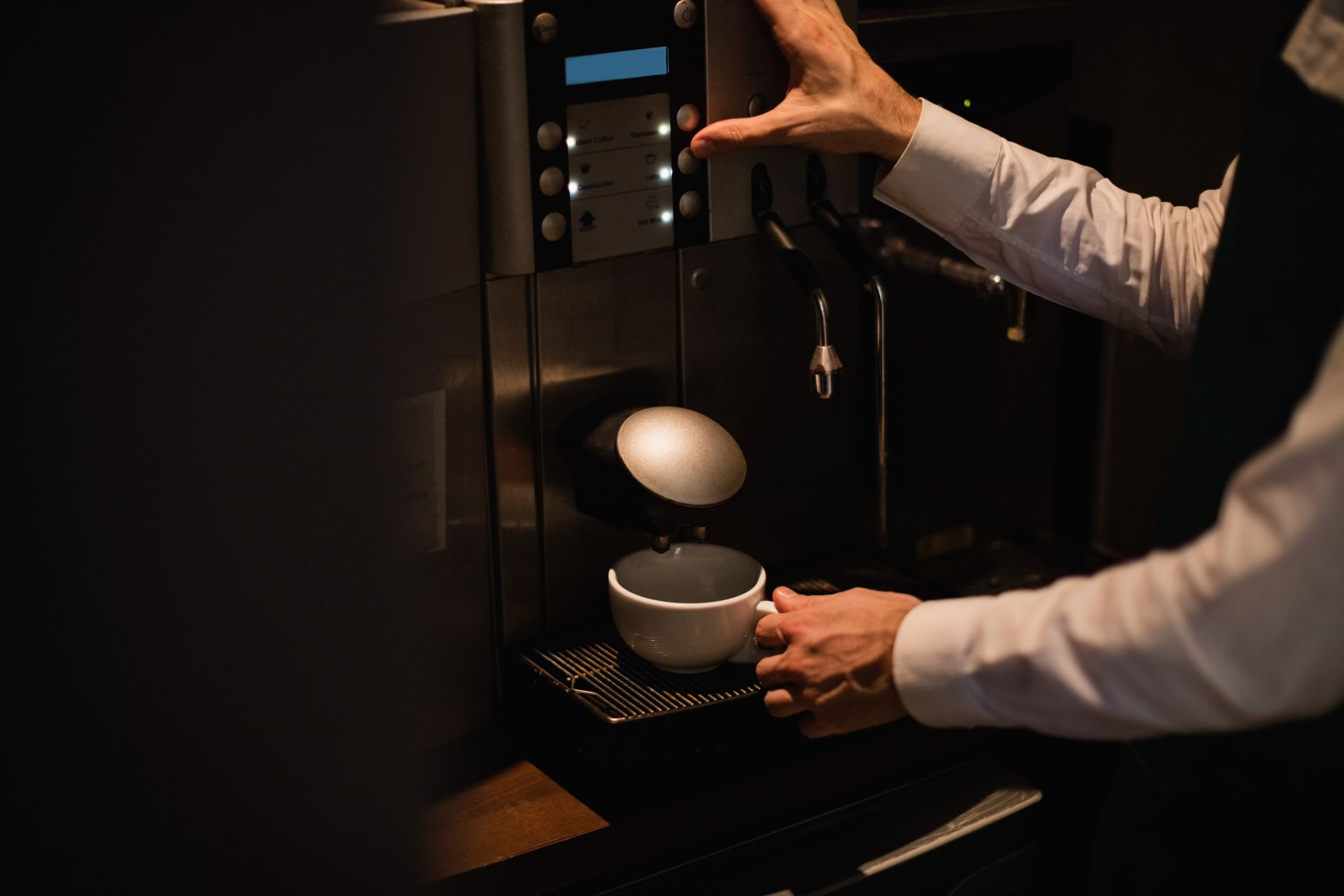 Persona con camisa blanca operando una máquina de café, vertiendo café en una taza.