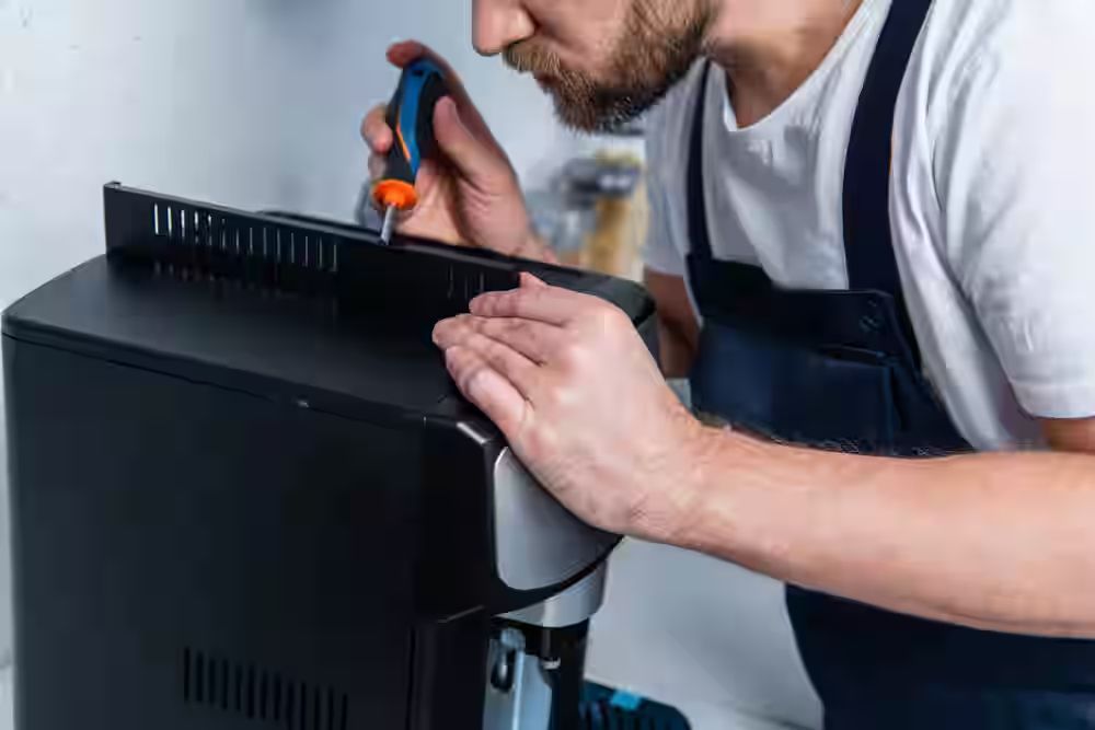 Persona que utiliza un destornillador para reparar una máquina de café negro.