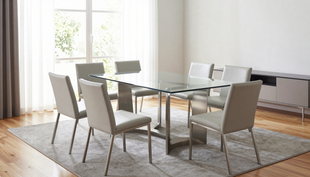 Sala da pranzo moderna con tavolo in vetro, sei sedie beige e luce naturale proveniente da un'ampia finestra.