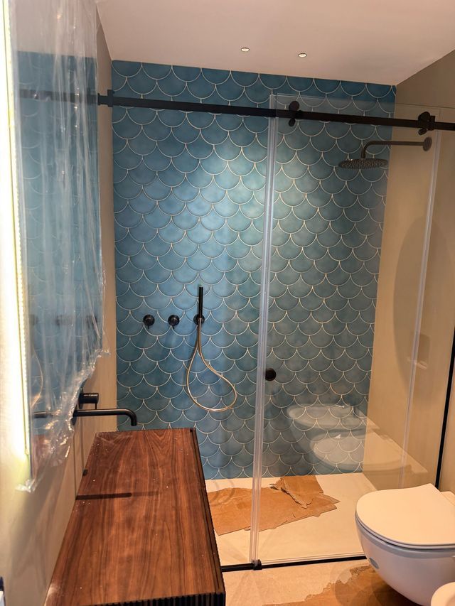 Bagno moderno con doccia in vetro, parete piastrellata di blu, mobile lavabo in legno e WC nelle vicinanze.