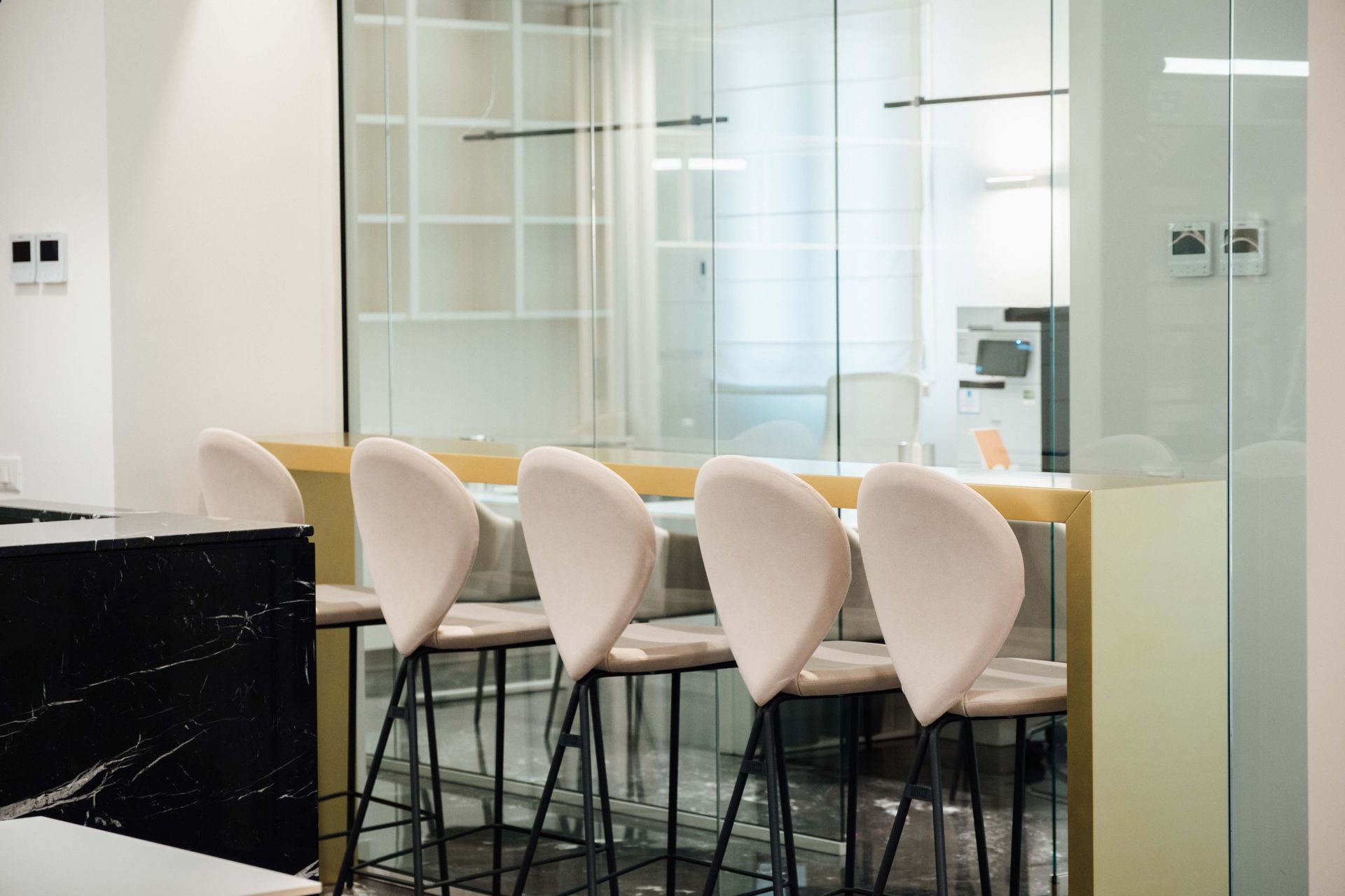 Moderna sala riunioni in vetro con tavolo bar, sgabelli bianchi e arredamento luminoso e minimalista.