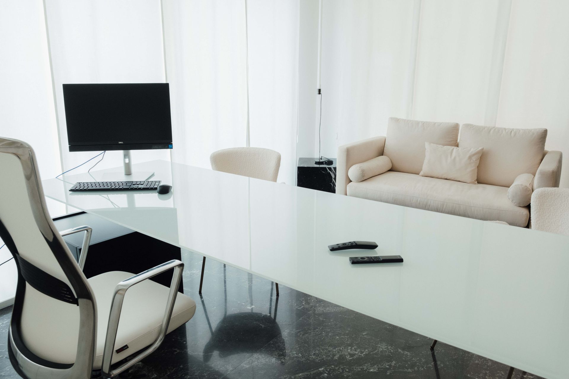 Sala conferenze moderna con tavolo bianco, divano beige e monitor per computer.