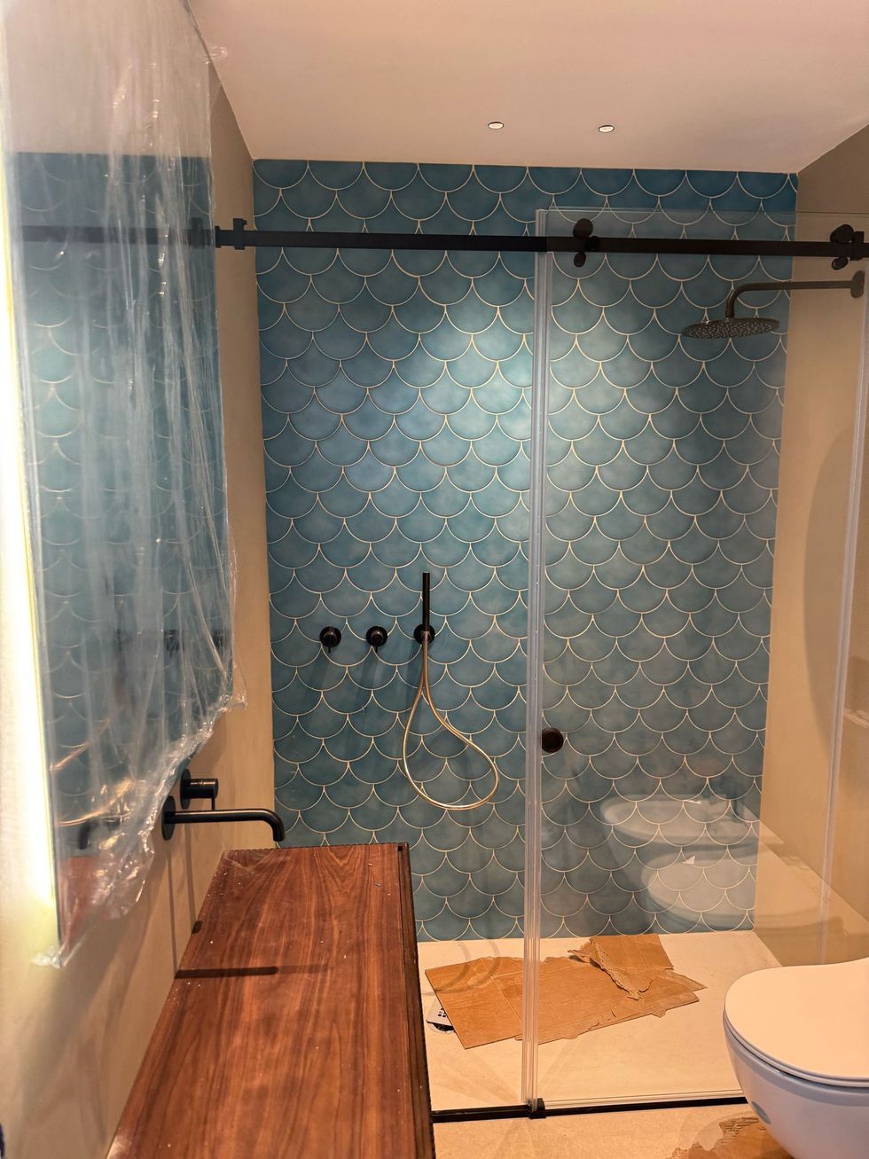 Bagno moderno con doccia piastrellata di blu, porta in vetro, mobile lavabo in legno e WC bianco in primo piano.