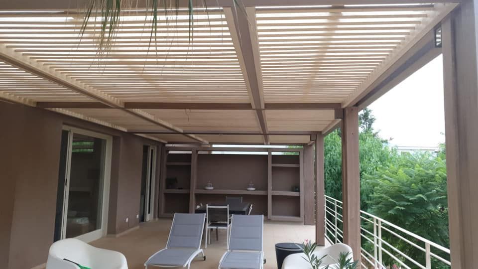 Patio con sedie a sdraio sotto un pergolato coperto accanto a una casa, con vista sul verde.