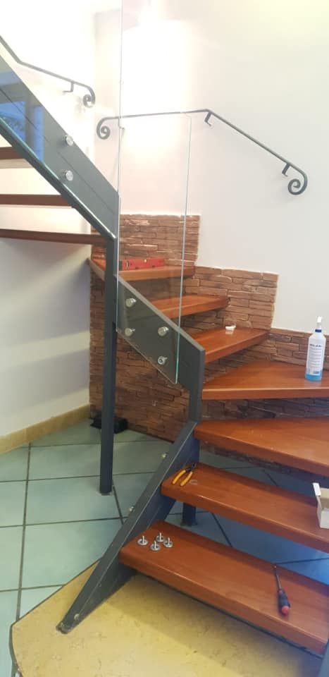 Scala interna con gradini in legno, ringhiera in vetro e un cesto di asciugamani piegati accanto al pianerottolo.