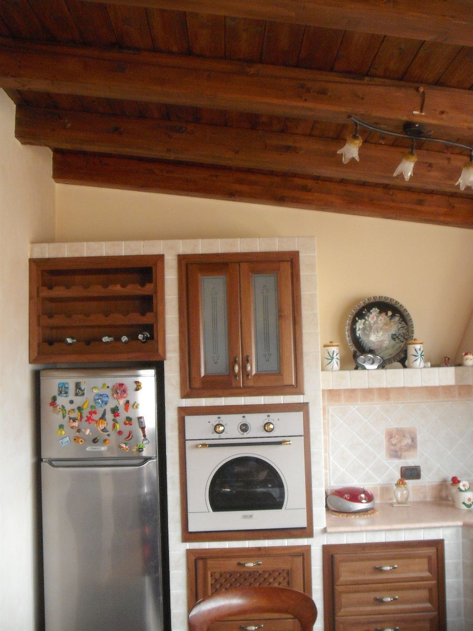 Cucina rustica con travi in legno a vista, frigorifero in acciaio inox, forno a incasso e mobili in legno.