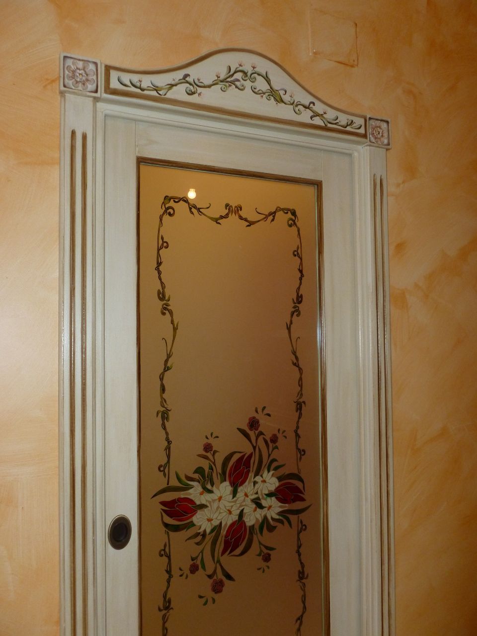 Porta bianca decorativa con motivi floreali e finiture ornate su una parete color pesca.