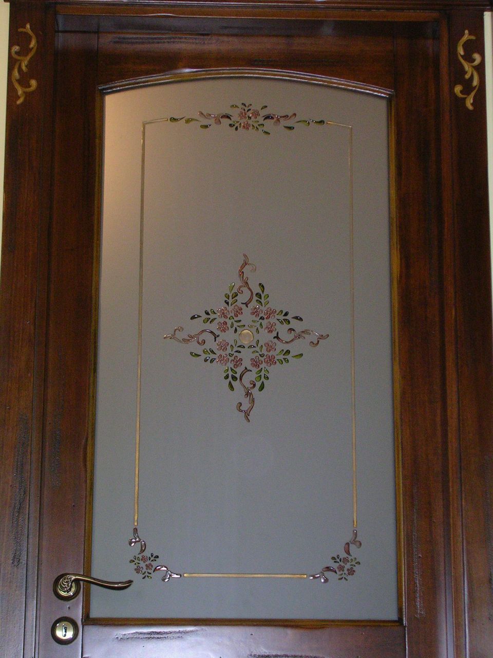 Porta d'ingresso in legno con pannello in vetro satinato e intarsio decorativo floreale, pomello e serratura in ottone.