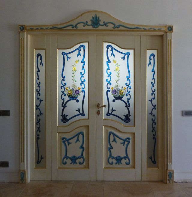 Doppie porte color crema decorate con pannelli in vetro blu a motivi floreali e dettagli dorati in un atrio