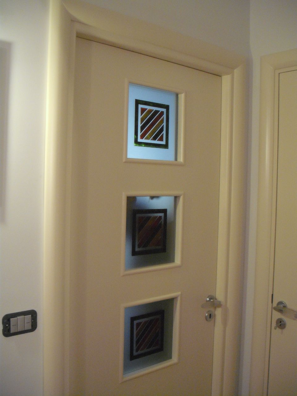 Porta interna color crema con tre piccole finestre quadrate decorative e maniglia argentata in un corridoio
