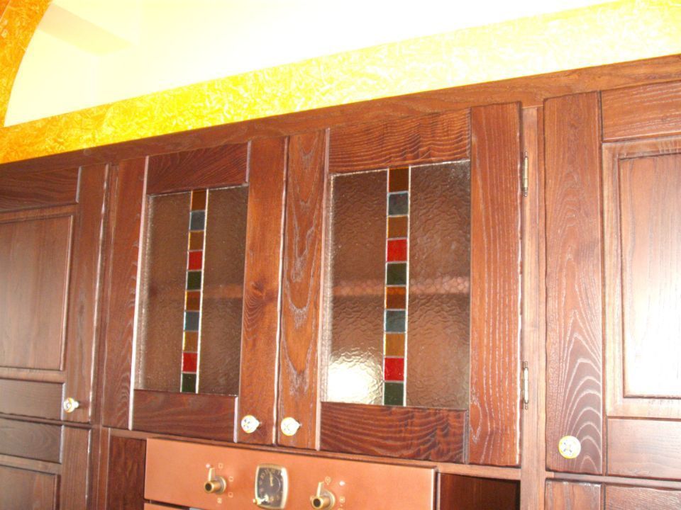 Mobili da cucina in legno con ante a pannelli di vetro e pomelli in ottone sotto una cornice a parete gialla.