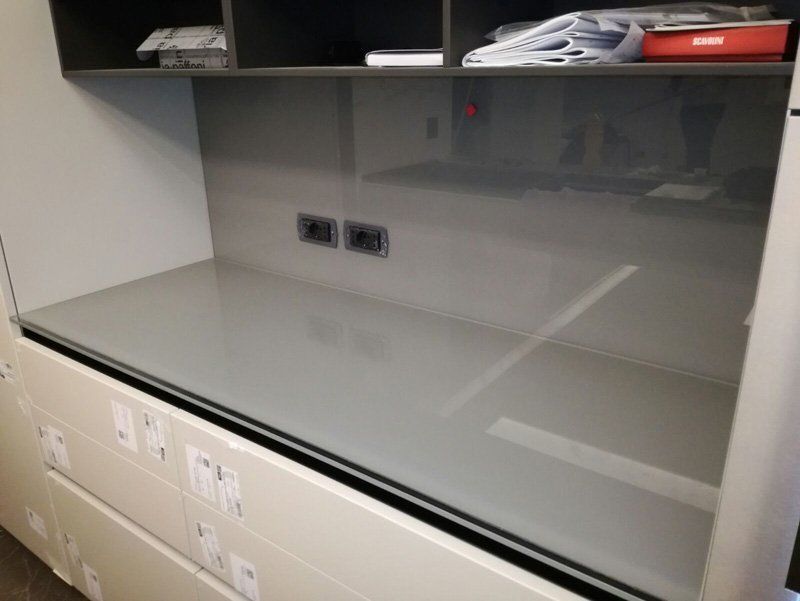 Scrivania moderna vuota con piano grigio lucido, mensole a muro e prese elettriche integrate.