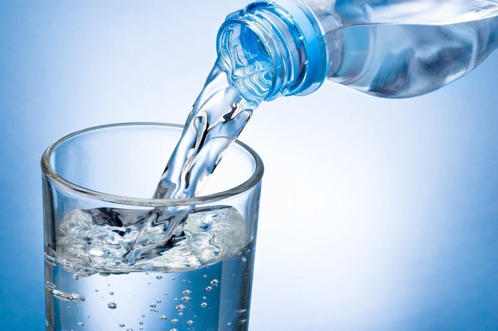 Water Being Poured From a Bottle Into a Glass, Blue Background — Port Macquarie Pure Water In Port Macquarie, NSW