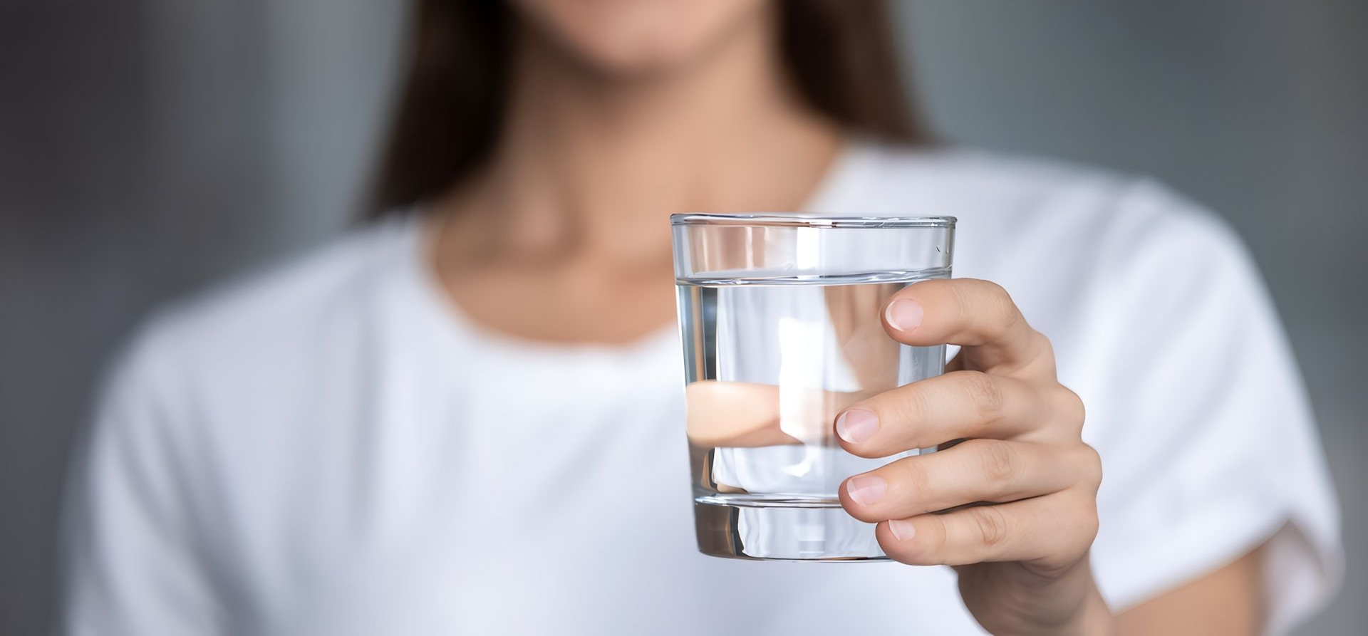 Woman Smiling, Holding Out a Clear Glass of Water — Port Macquarie Pure Water In Port Macquarie, NSW