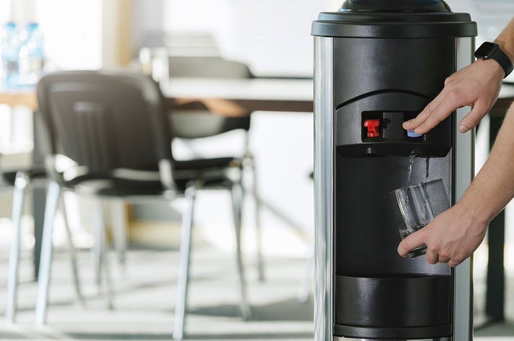Person Filling Glass With Water From a Water Cooler in an Office Setting — Port Macquarie Pure Water In Port Macquarie, NSW