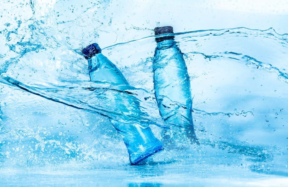 Two Blue Plastic Water Bottles Amidst Splashing Water — Port Macquarie Pure Water In Kempsey, NSW