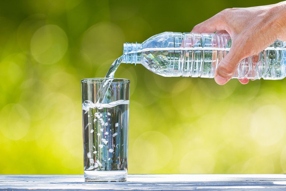 Hand pouring water from a plastic bottle into a clear glass — Port Macquarie Pure Water In Port Macquarie, NSW