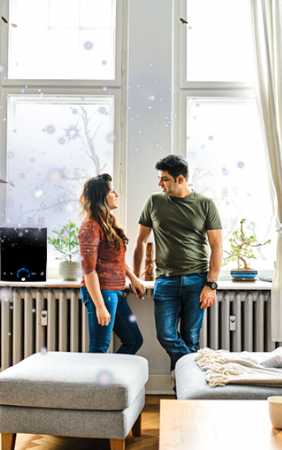 Two people talking beside a bright window in a modern room with a radiator and potted plant.