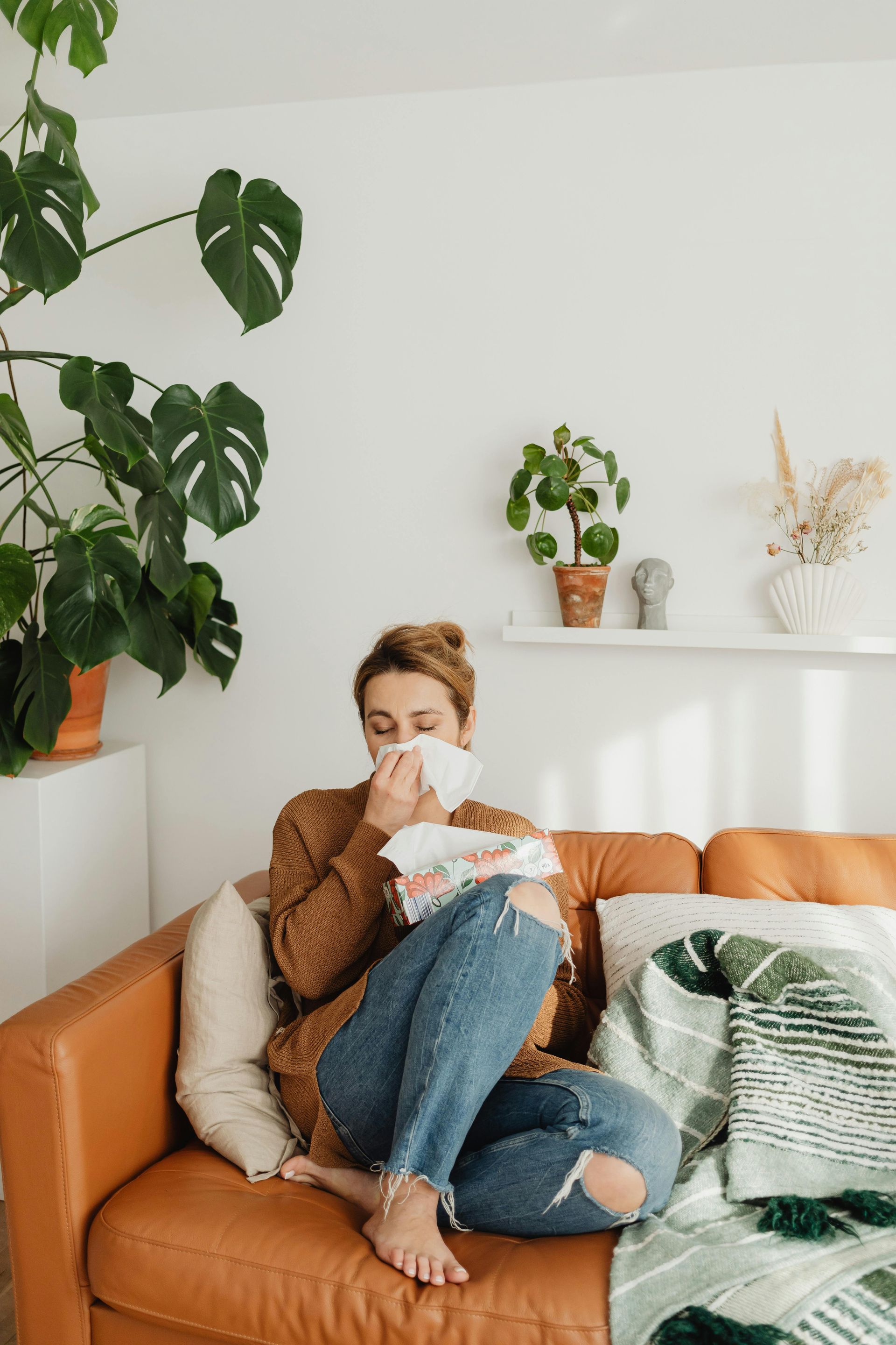 Person wrapped in a blanket sitting on a couch and drinking from a mug in a cozy living room