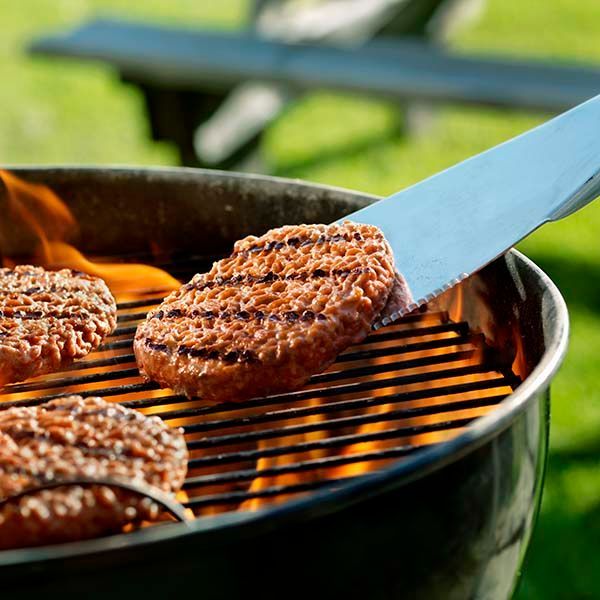 Grilled burger patties on a barbecue, with one being flipped by a metal spatula.