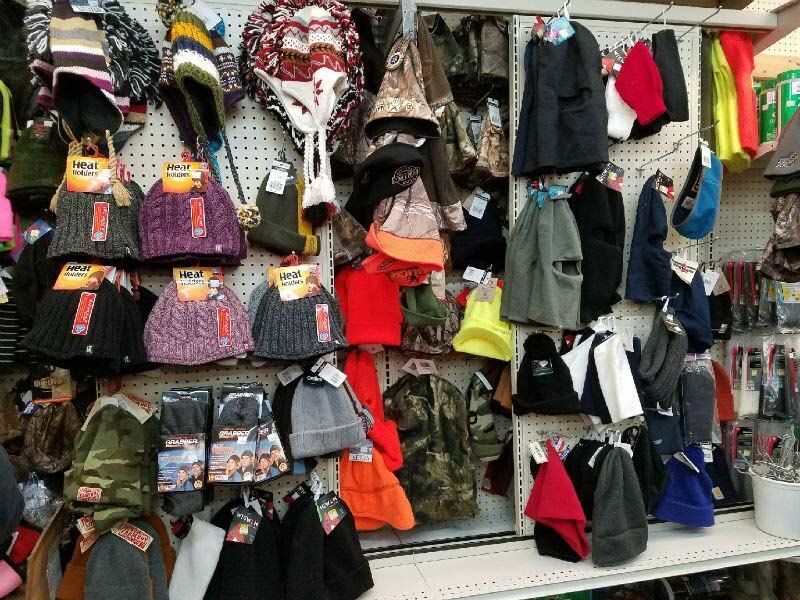 Market stall displaying colorful hanging bags, hats, and clothing on a wall display.