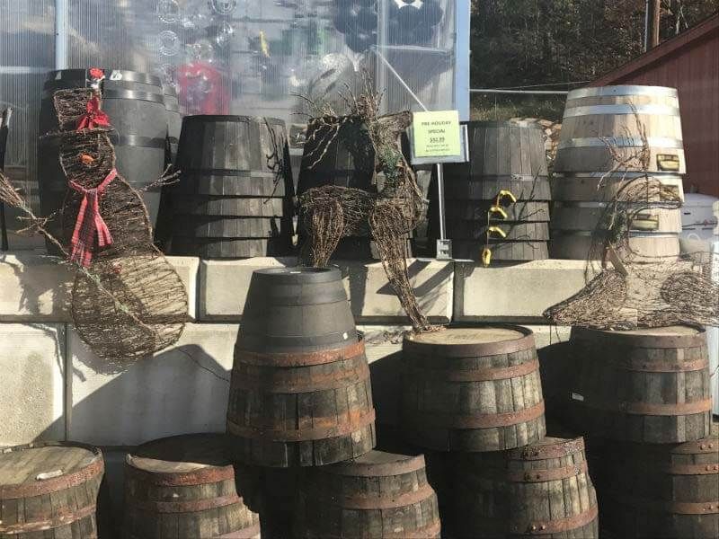 Stacks of black and brown barrels outside a storefront, with camouflage nets and a small sign in the window