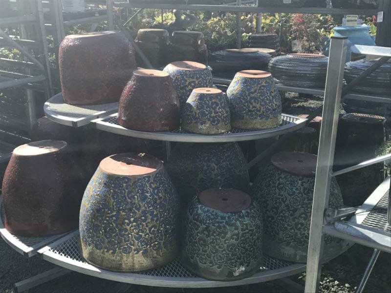 Stacked ceramic planters in various colors displayed outdoors on metal racks.