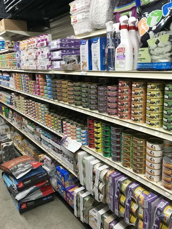 A pet store aisle with stacked cans and bags of pet food on metal shelves.