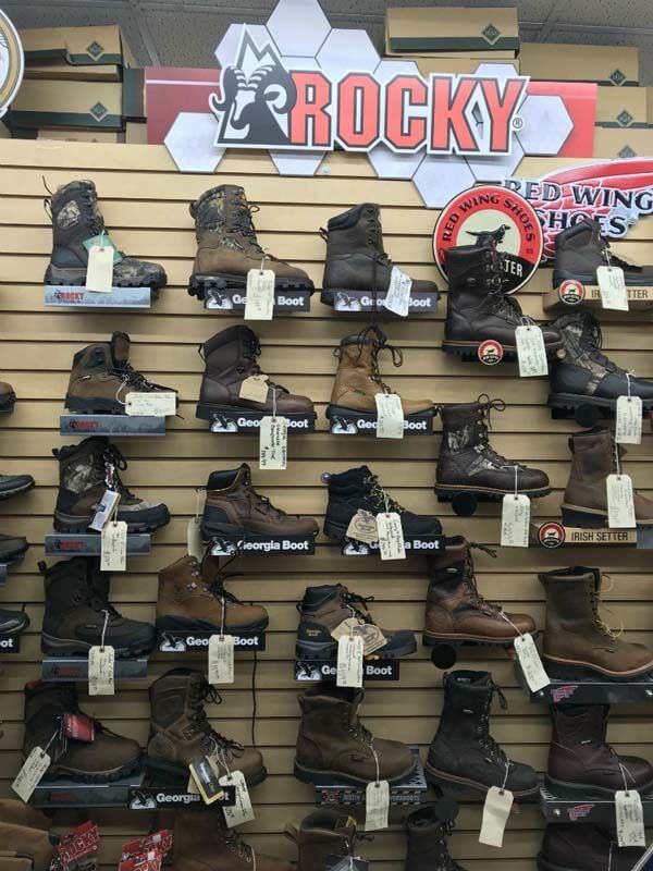 Wall display of many hiking boots and shoes beneath a large Rocky sign in a store.