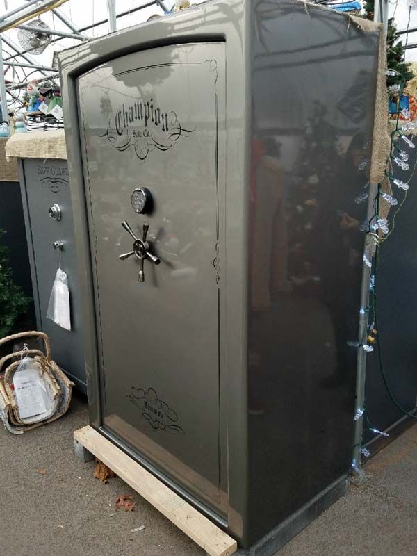 Gray metal gun safe with decorative door and combination lock, shown outdoors at a market stall