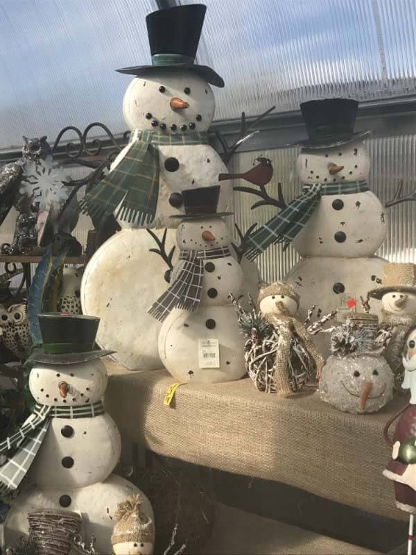 Decorative snowmen with black hats and plaid scarves arranged on a porch bench in winter